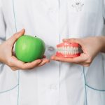 A false denture and a green apple in the hands of a dentist. Dental prosthesis care